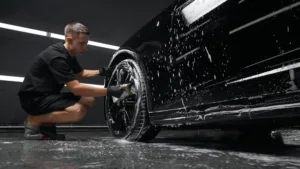 Technician washing car wheel during foam detailing in service bay
